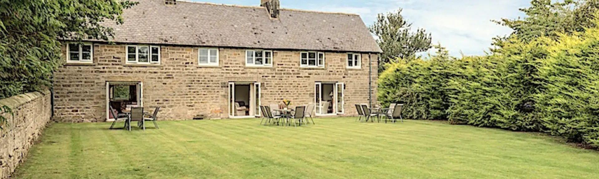 A long, stone-built cottage with 3 floor-to-ceiling ground-floor windows overlooking a spacious lawn. 