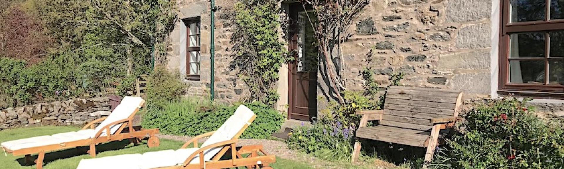 Sun loungers on a lawn in front of a stone-built holiday cottage