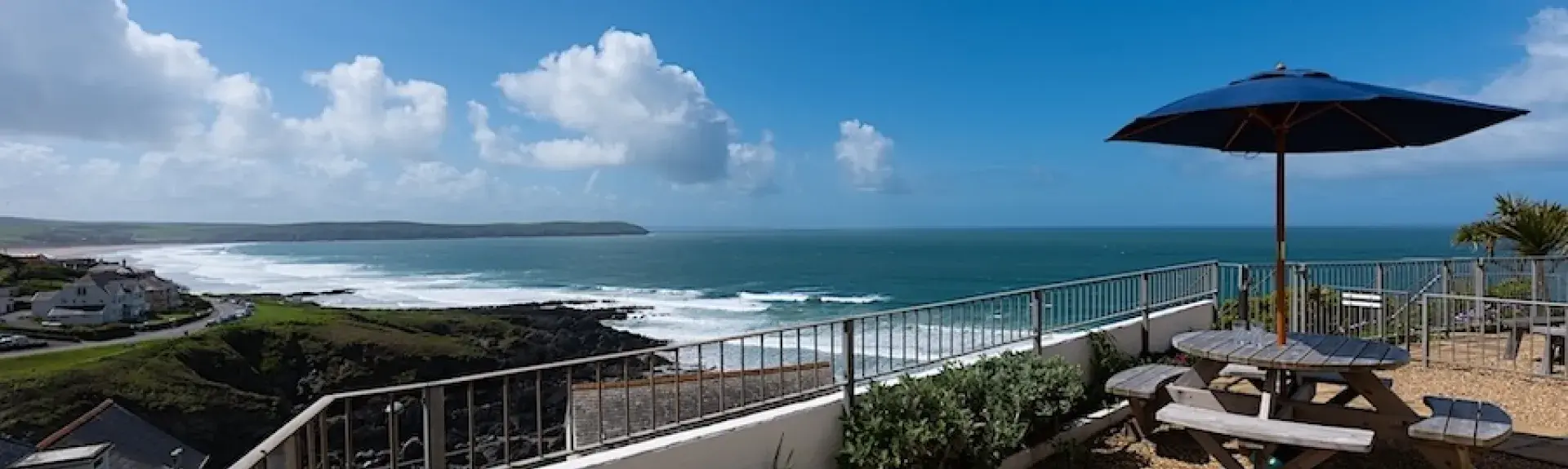 A view from sun loungers on a balcony to surf breaking on a beach in the distance.