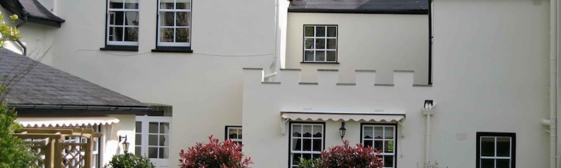 A large Regency cottage with large sash windows overlooks a flower-filled garden.