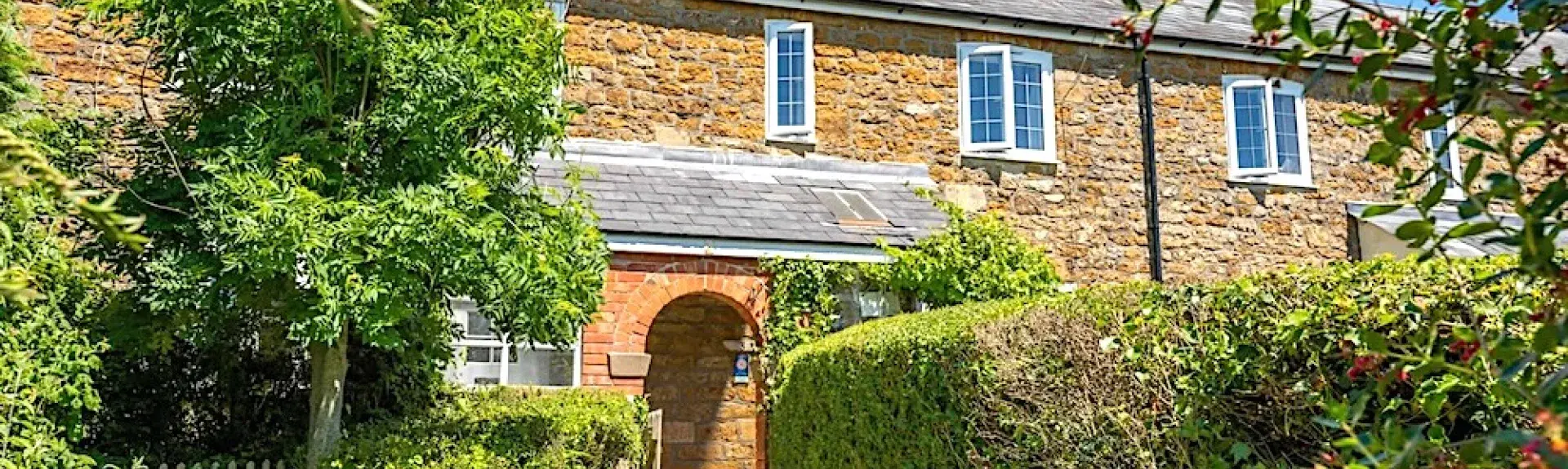 A footpath flanked by privet hedges leads to a stone-built holiday cottage with a covered porch.