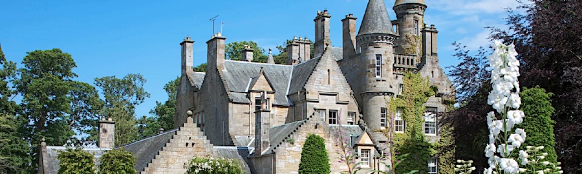 A multi-turreted Scottish castle in landscaped gardens.