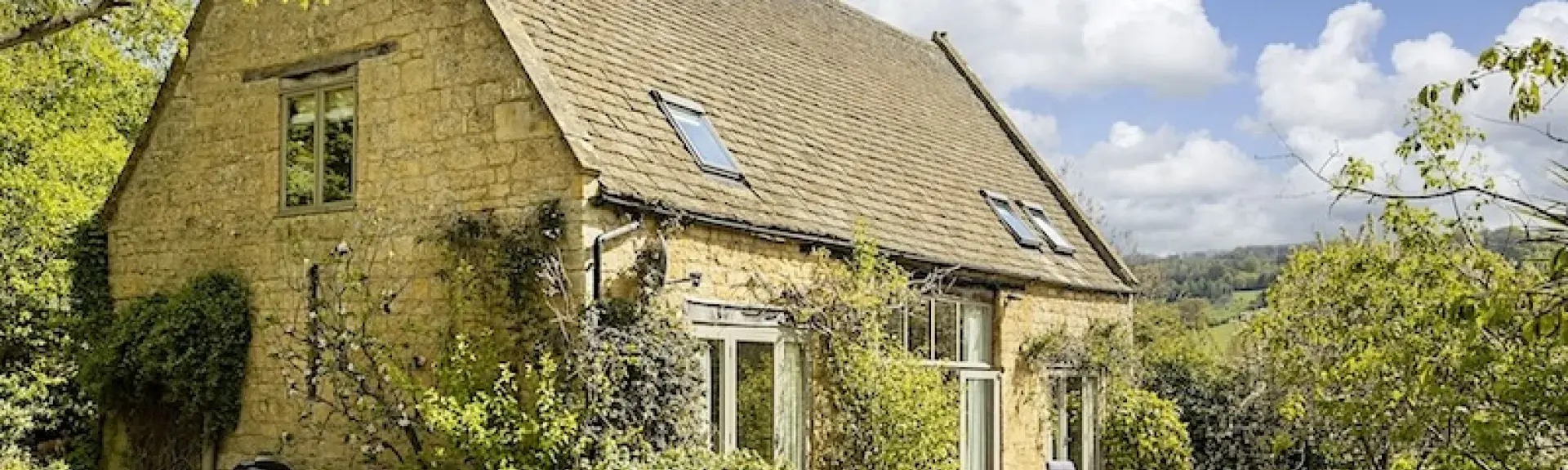 Cotswold Barn conversion surrounded by trees and shrubs.
