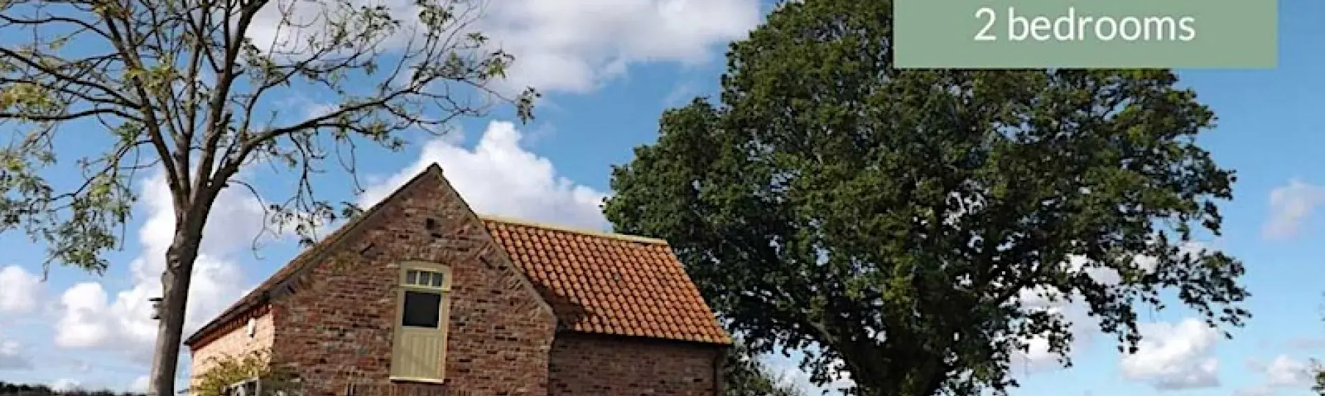 A brick-built cottage nestles between two trees overlooking open countryside