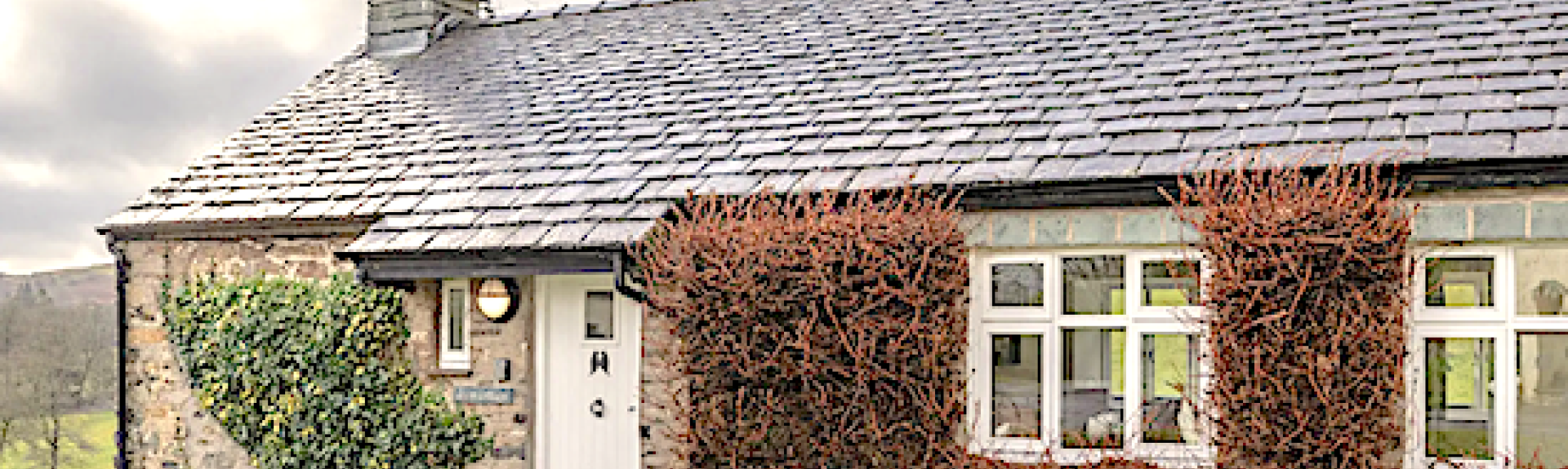 A stone-built,single storey holiday cottage with vine covered walls and a front garden.