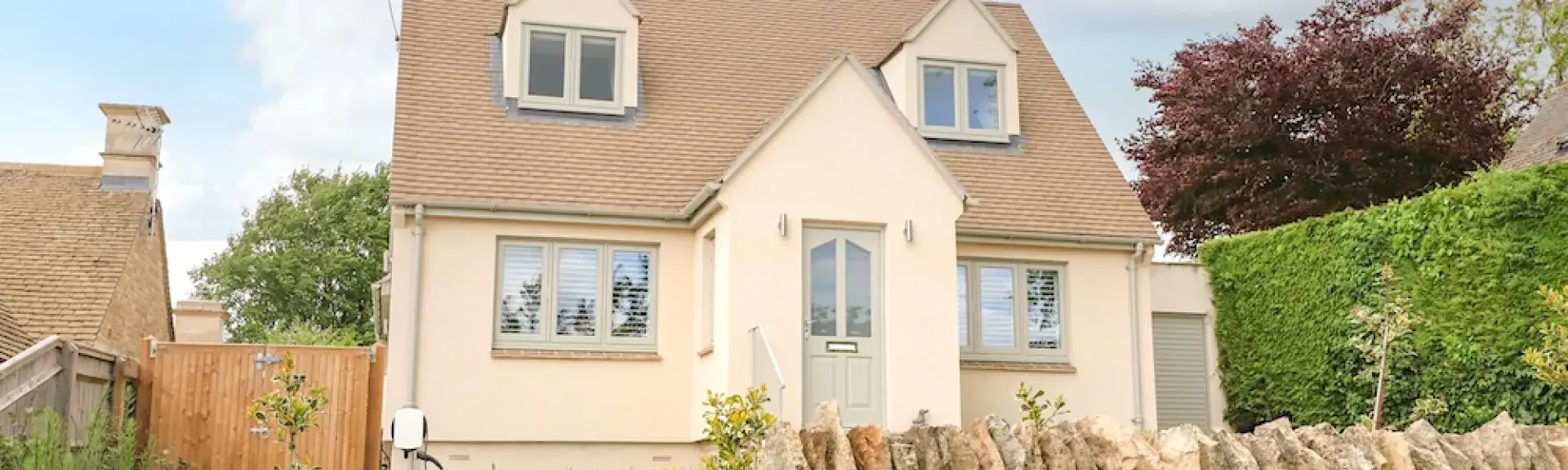 Exterior of a contemporary detached village house behind a dry stone wall.
