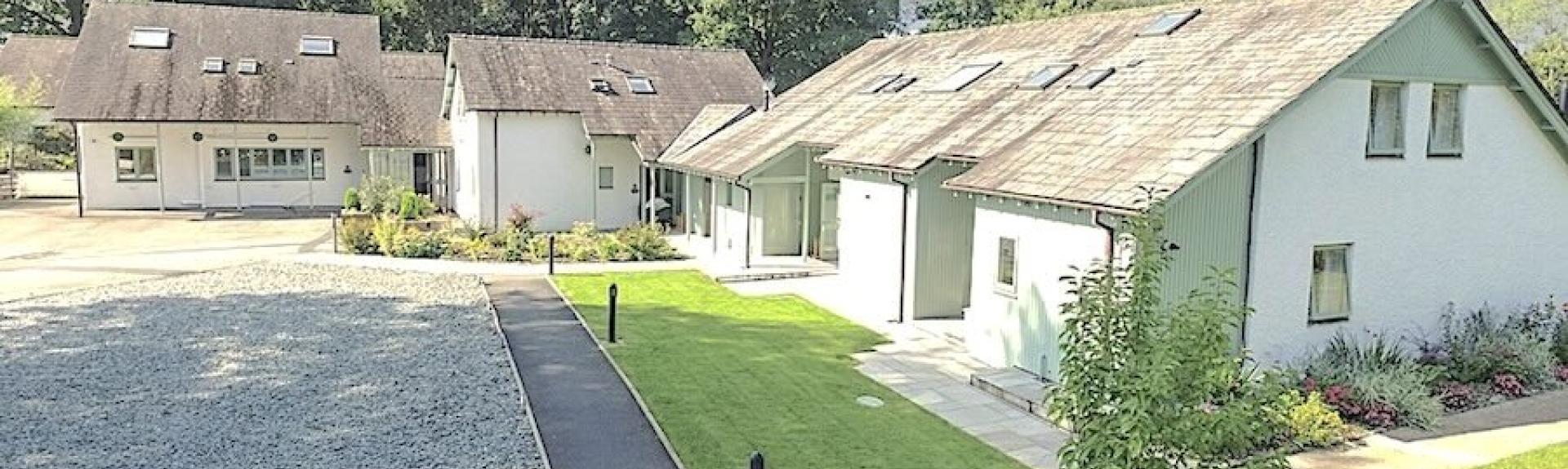 A chalet bungalow in Windermere overlooks a front lawn and a large parking area.