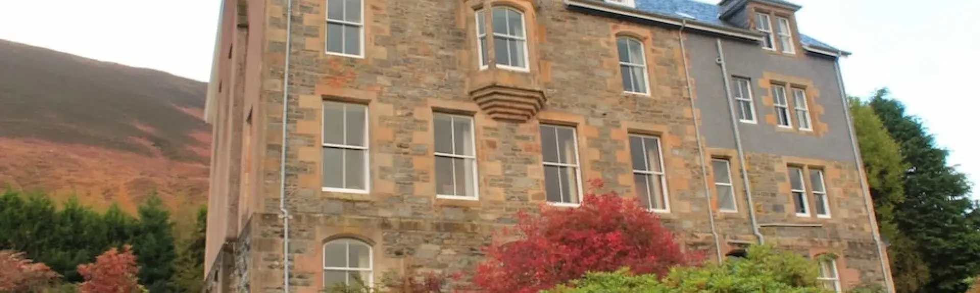 Exterior of a grand 3-storey Highland hunting lodge and gardens.