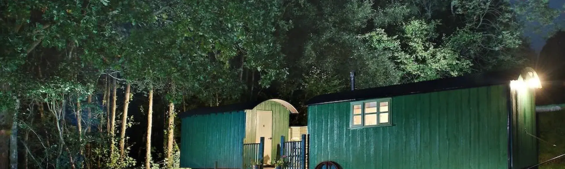 Two shepherd huts at dusk, converted and linked to form a single unit.