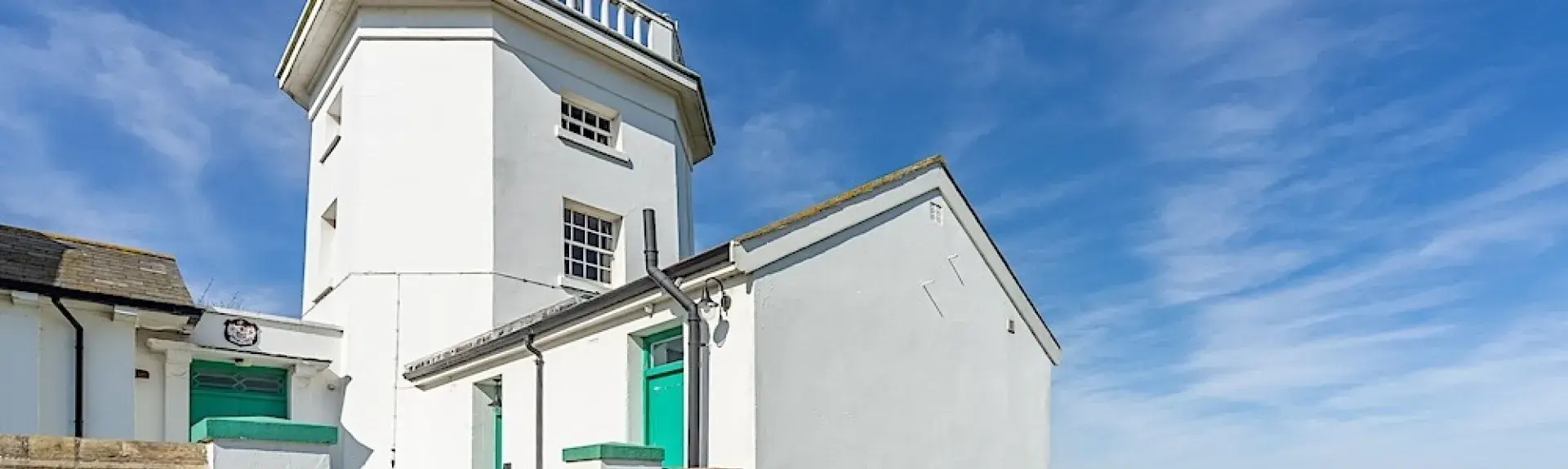 Exterior of a lighthouse holiday cottage and small tower on a grassy clifftop