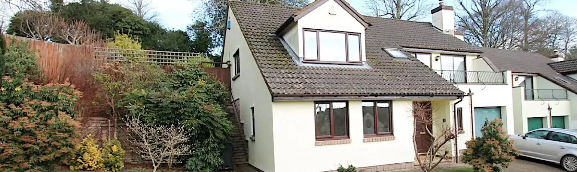 A modern 2-storey Exmoor house with a glass-fronted balcony and a lawn dotted with small trees