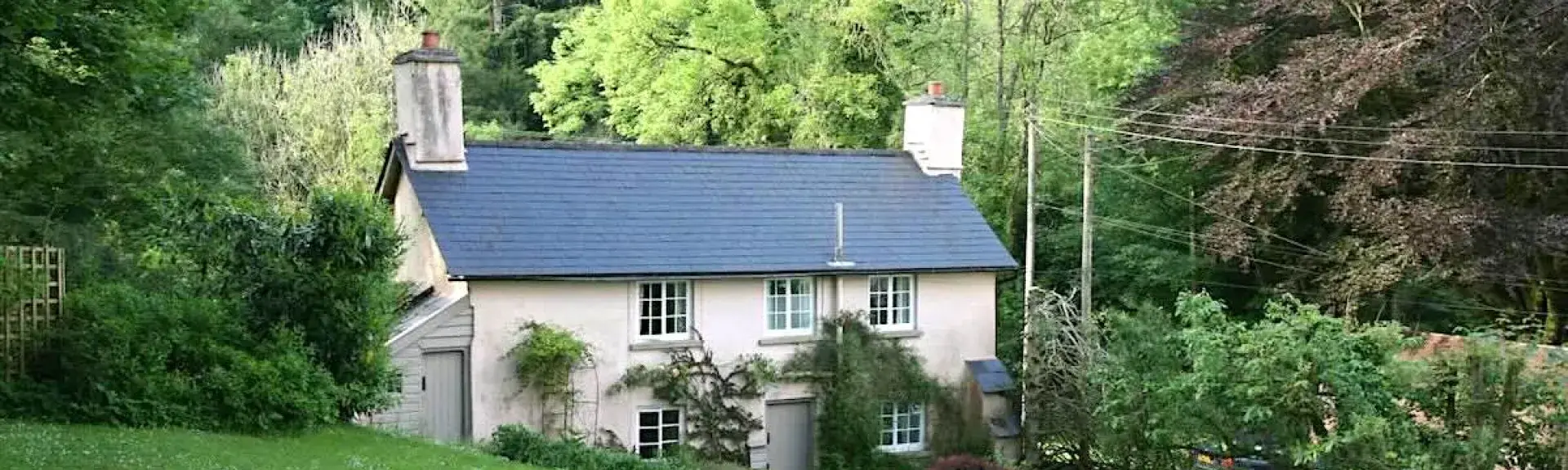 Double-fronted cottage with large lawn surrounded by mature trees.