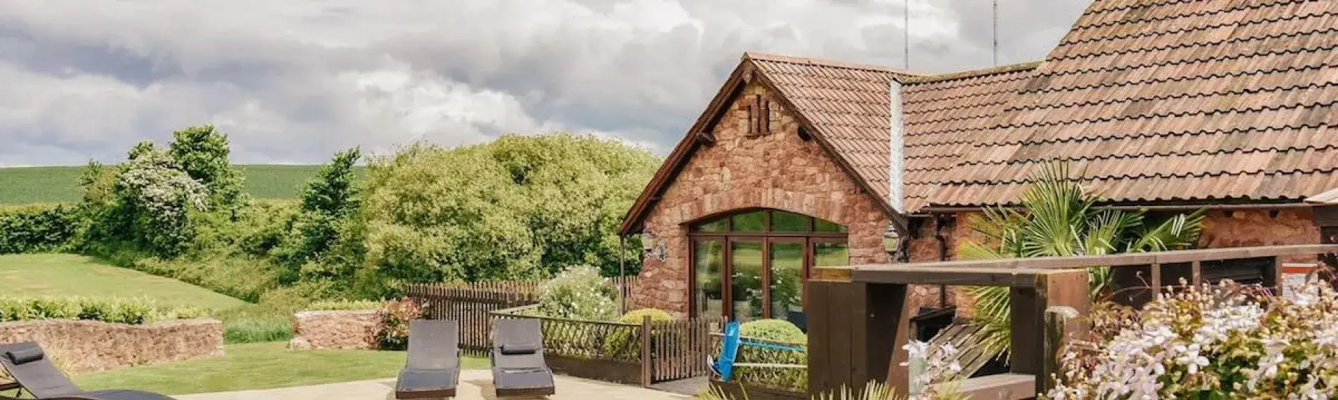 A stone barn conversion overlooks an outdoor swimming pool in a shrub-filled garden