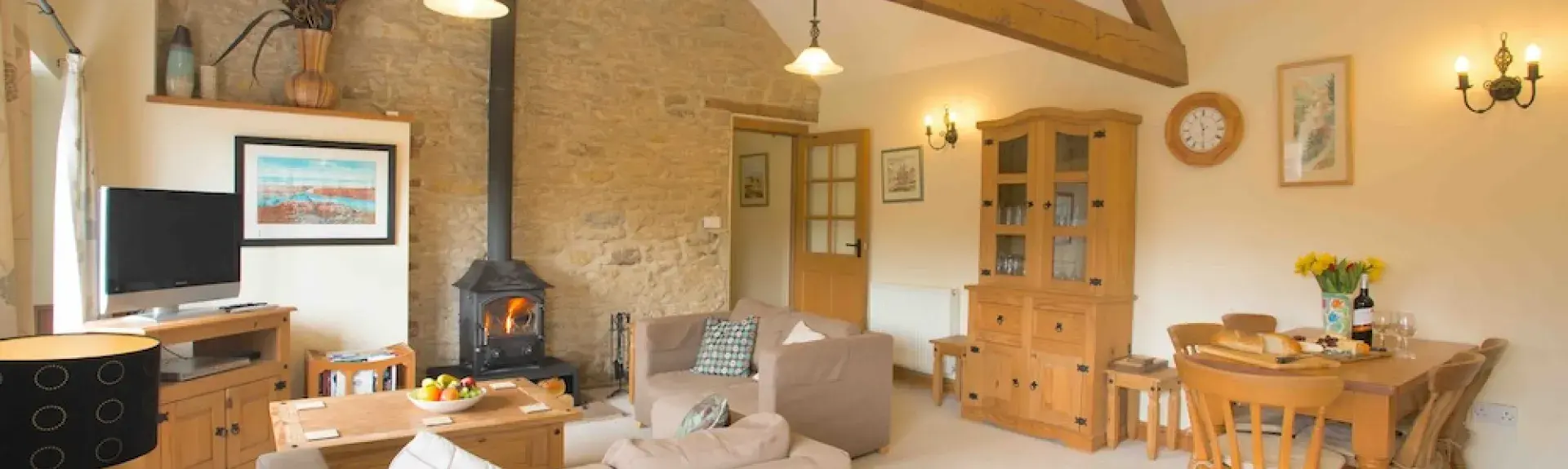 A spacious, oak-beamed lounge area with sofas, TV, wood burner and dining table.