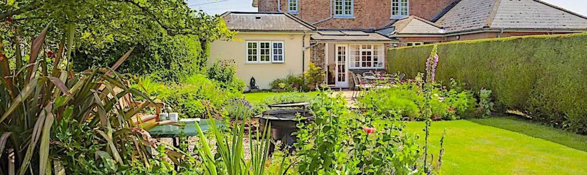 A brick house overlooks a large lawn with flower-filled borders