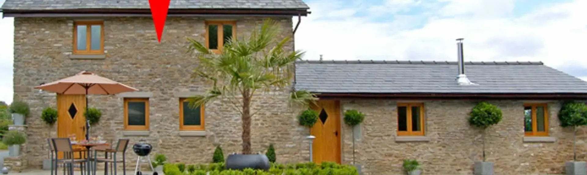 A stone-built Wye Valley holiday cottage overlooks a paved patio with dining furniture.