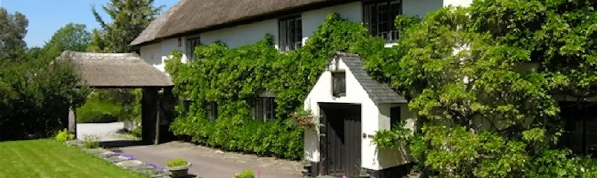 A large, thatched, wisteria-clad Somerset holiday cottage with a covered porch.