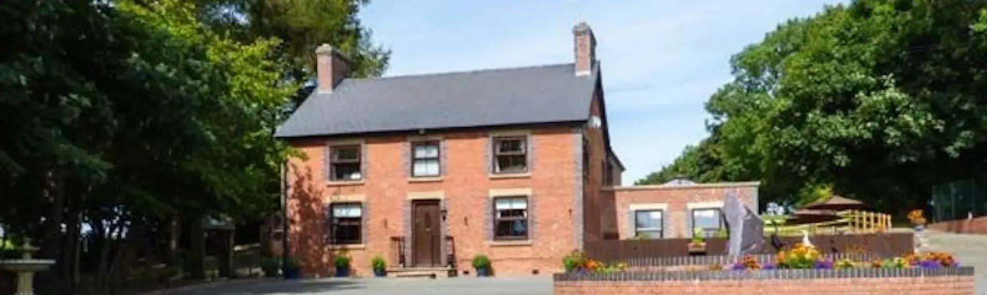 Exterior of a large, double-fronted brick cottage with a spacious parking area and gardens.