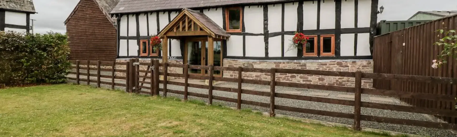 A historic 'black-white white' timbered Herefordshire farm cottage sits behind a terraced and fenced-in lawn.