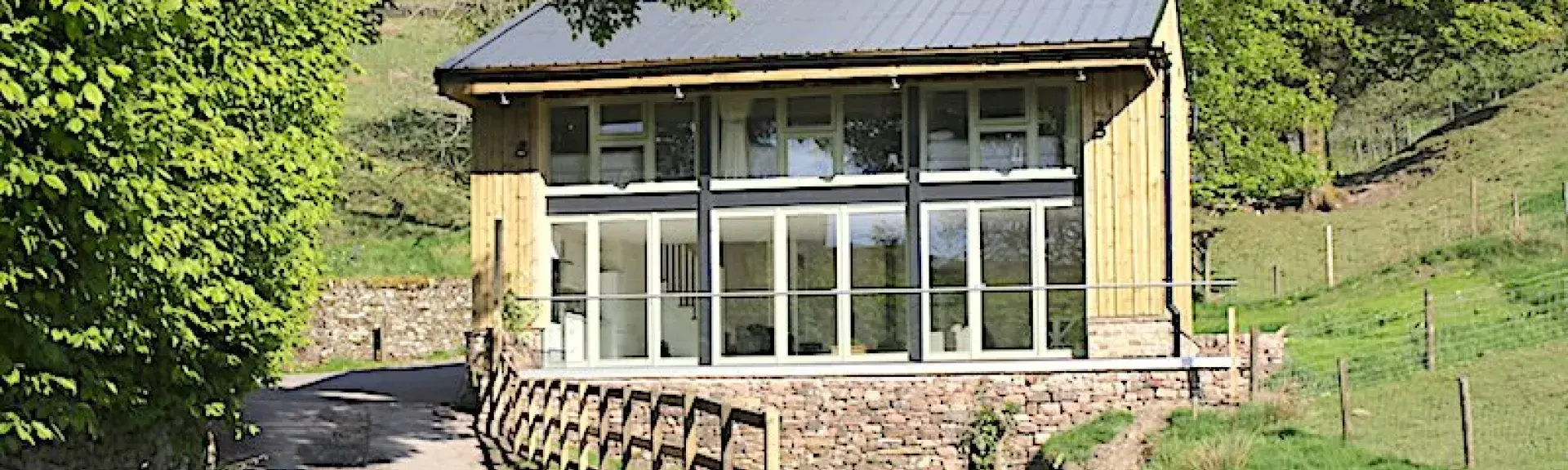 Exterior of a contemporary country cottage with a full-width balcony and floor-to-ceiling bi-fold glass doors.