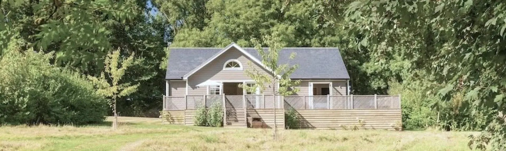 On the edge of a mature wood, a timber-frame lodge with a spacious deck overlooks an open field.