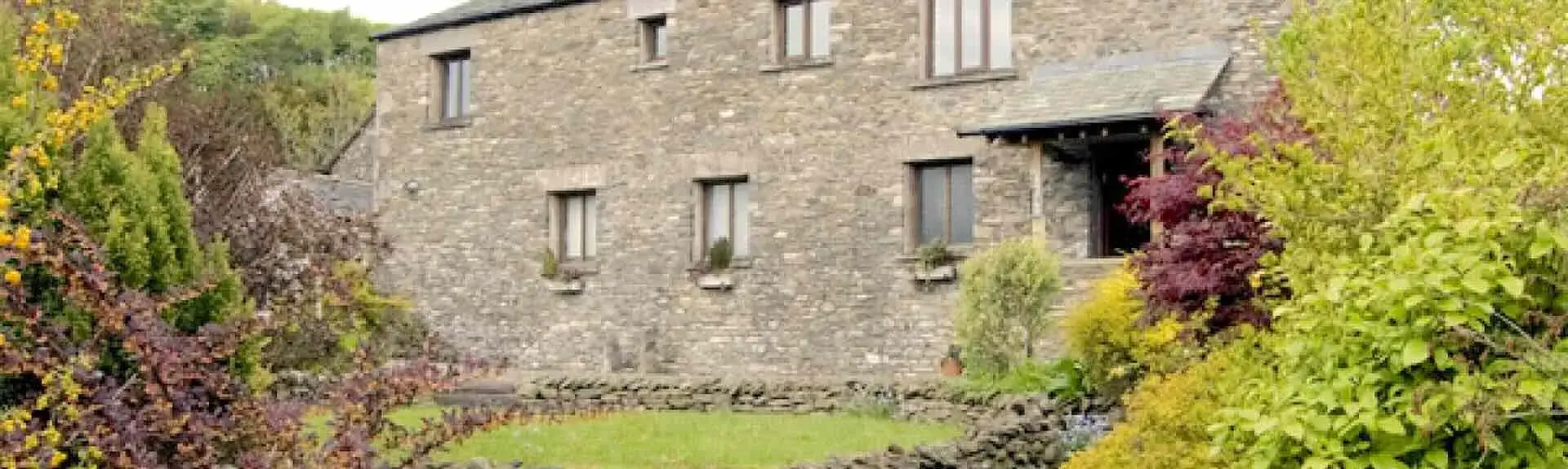 A barn conversion in Kendal overlooks a lawn surrounded by mature shrubs and bushes.
