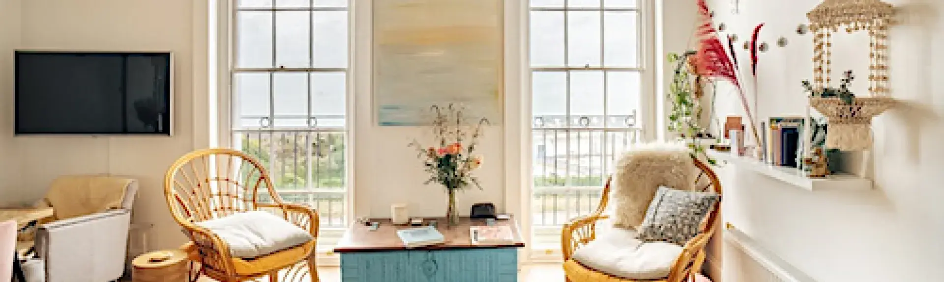 A wood floored lounge with wicker arm chairs and sea views through floor-to-ceiling windiows.