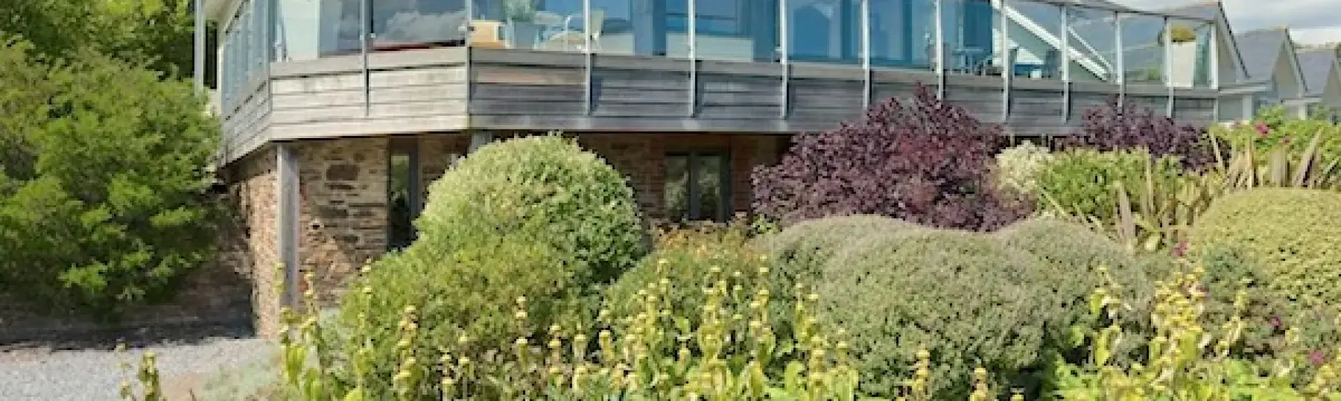 A contemporary wood and glass bungalow with a wrap-around deck overlooks a shrub-filled garden.