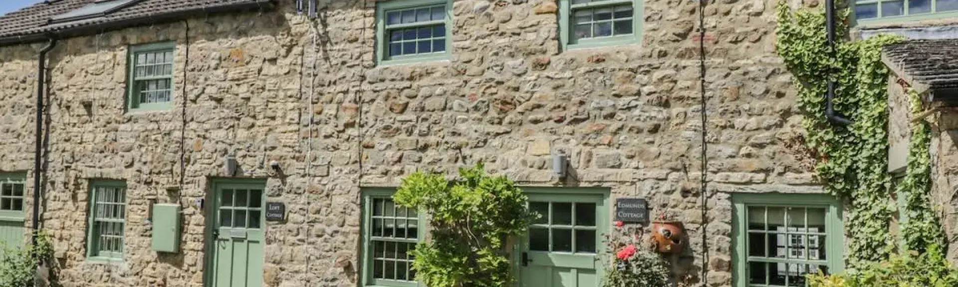 A terrace of 3-stone-built Bedale holiday cottages facing a lawn.