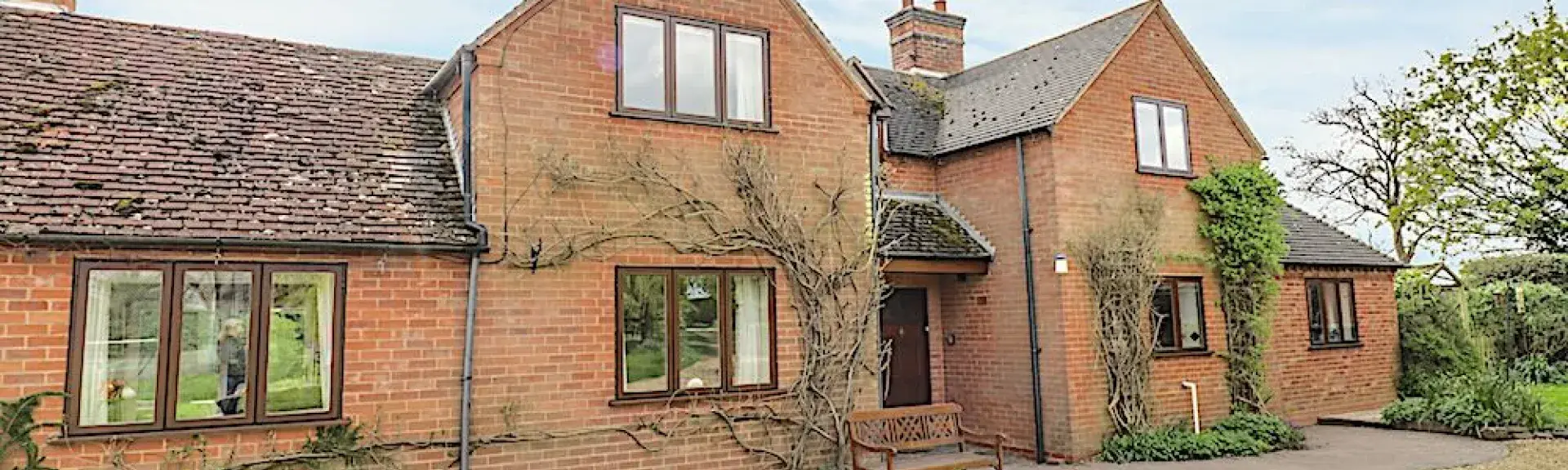 A twin-gabled brick house with large windows sits behind a shingled drive.
