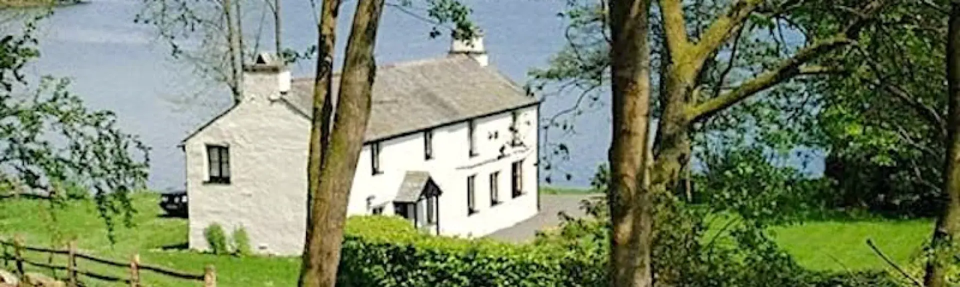 Exterior of a large 2-story house surrounded by a lawn on the shores of a large lake.