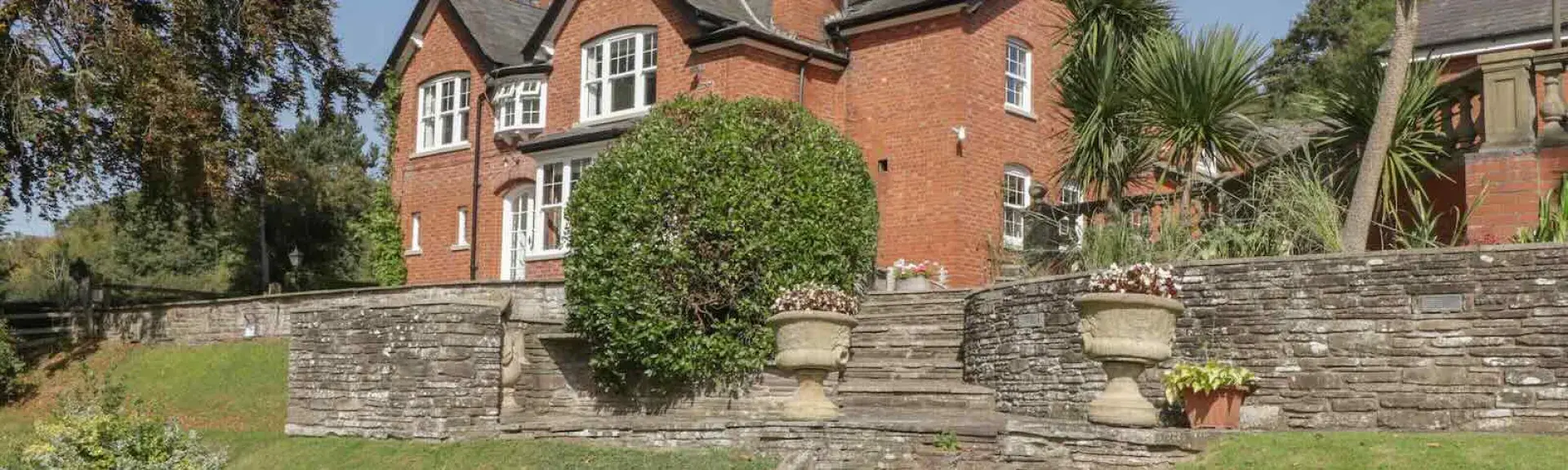 A large brick house backed by tall pine trees overlooks an extensive lawn.