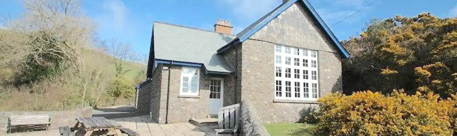 A converted stone-built, remote Exmoor schoolhouse with a lawn and large patio.