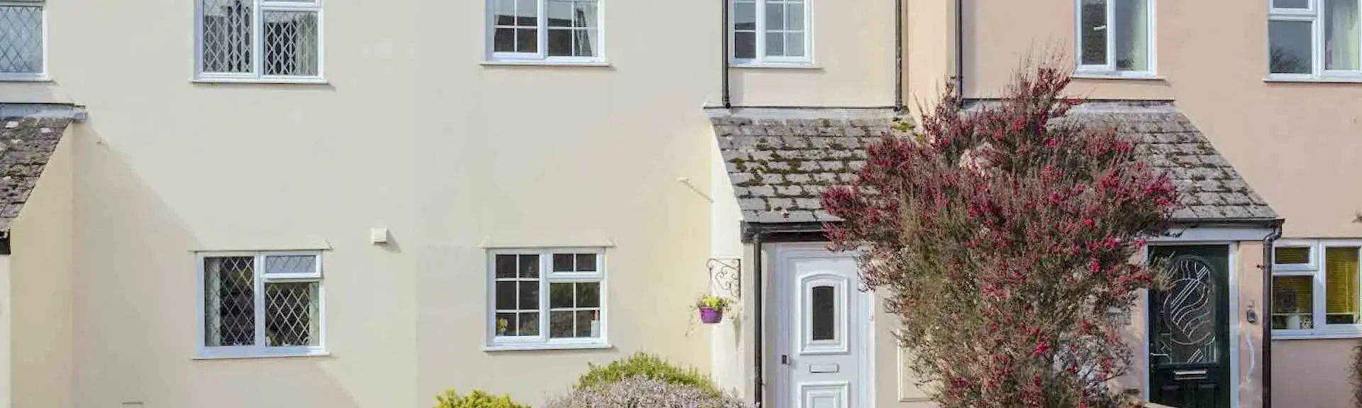 A gable-windowed holiday cottage faces a large lawn bordered by bushy shrubs.