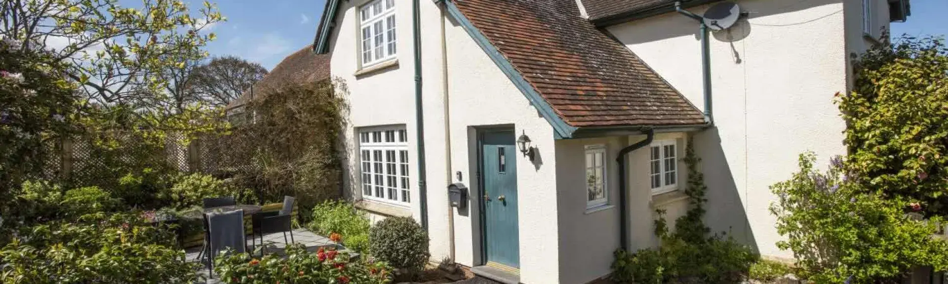 The exterior of a detached Somerset holiday cottage and shrub-filled garden.