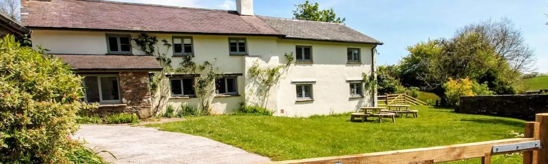 Large Exmoor holiday cottage overlooks a spacious lawn and a drive with a wooden 5-bar entry gate.