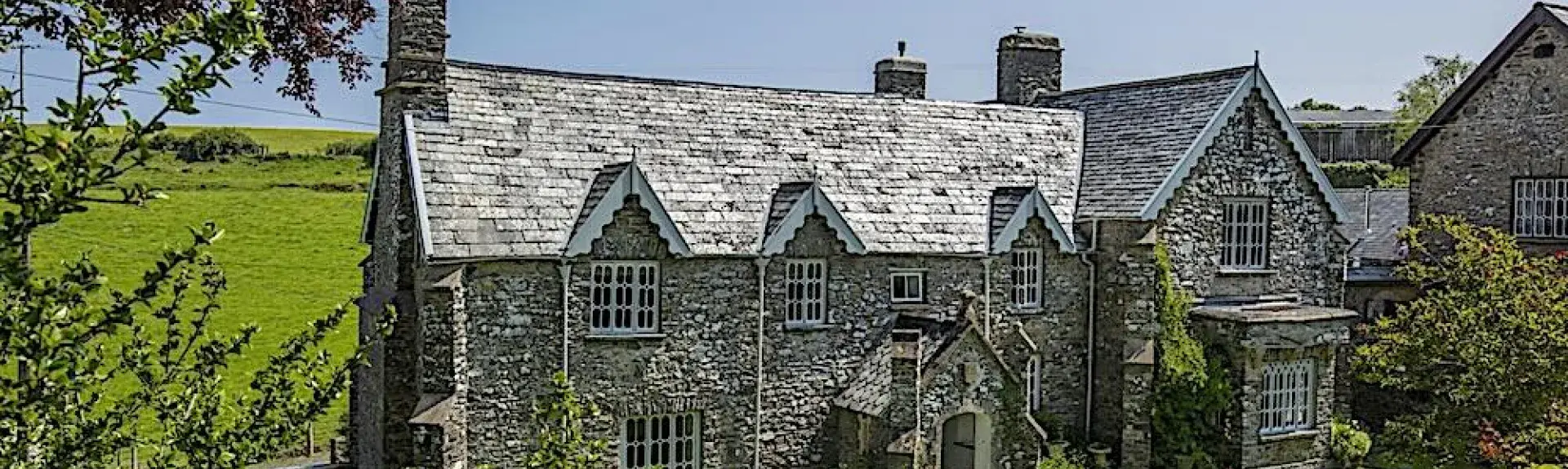 A large stone-built Exmoor cottage surrounded by trees and open fields.
