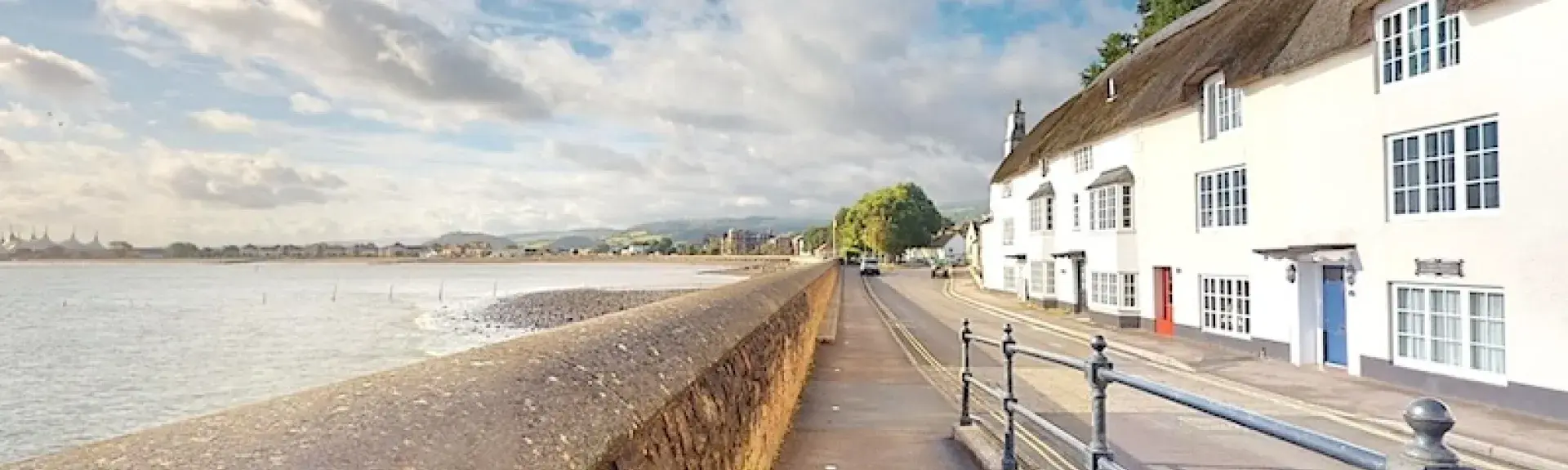 A terrace of thatched cottages overlooks a road and beachfront at low tide.