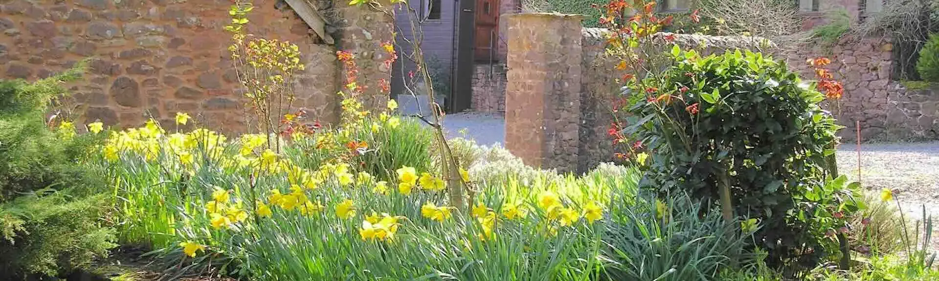 Exterior of a stone-built holiday home in Dunster surrounded by a stone wall..