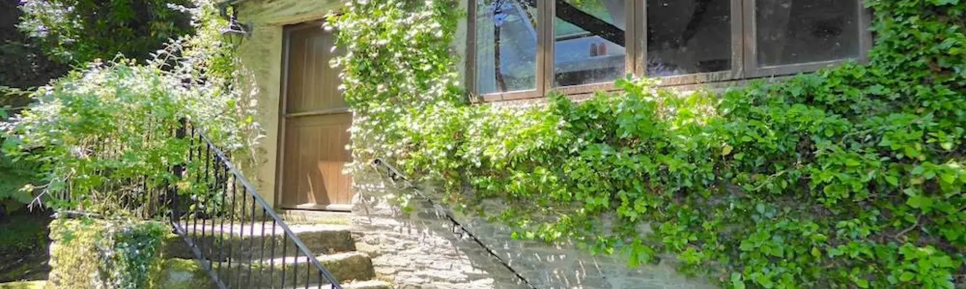 The leafy-clad exterior of a stone-built single-storey Exmoor holiday cottage with a flight of stone steps to the front door.