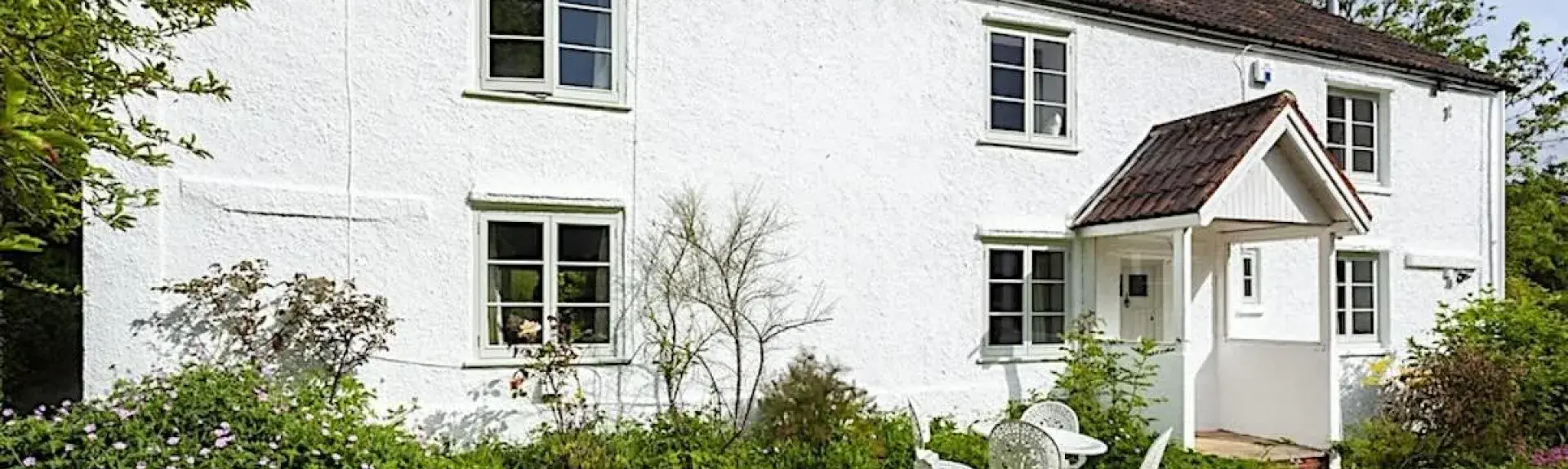 A Somerset farmhouse overlooks a large lawn lined by shrubs.