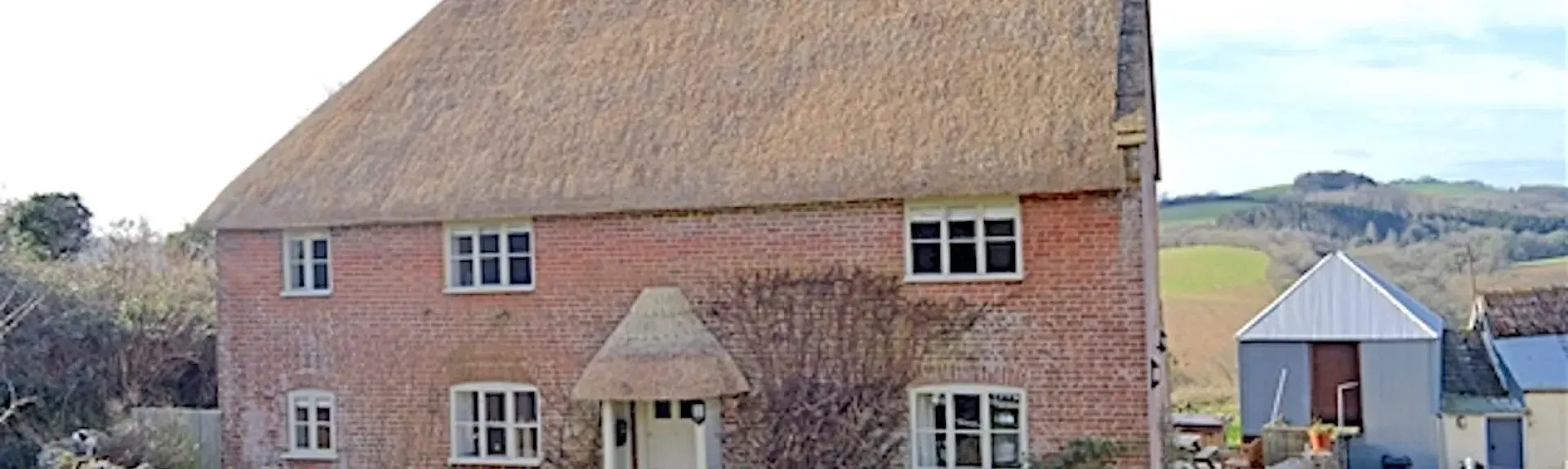A Thatched farmhouse with a garden surrounded by a picket fence.