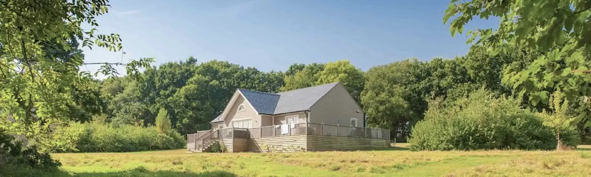A single-storey eco-lodge surrounded by a deck and open fields.