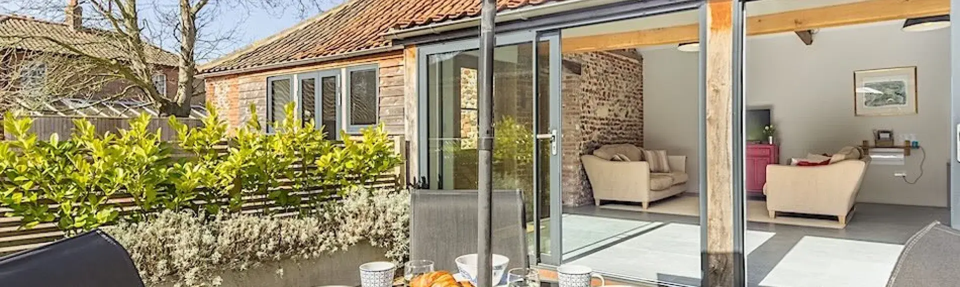 A single-storey barn conversion with folding French windows opening onto a dining terrace.