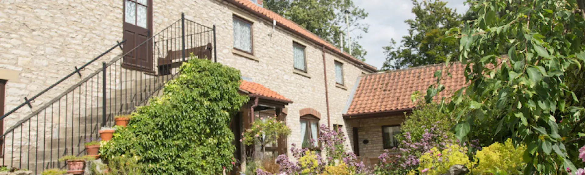 Exterior of a large barn conversion with external steps to 1st flor front door - facing a mature garden