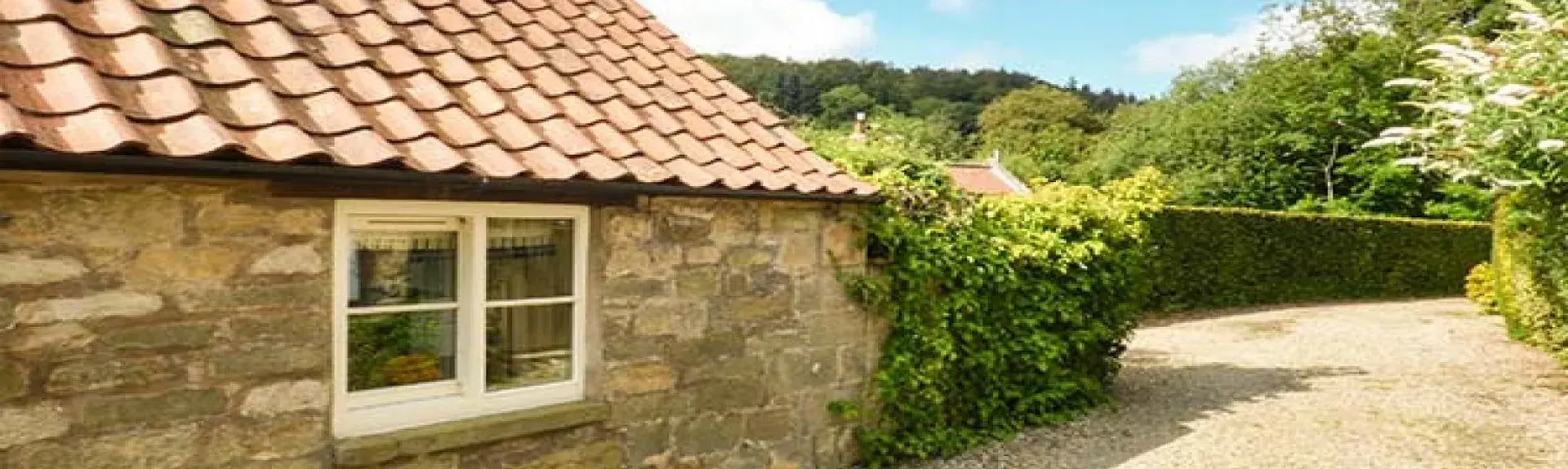 A semi-detached cottage with an enclosed front porch and a front garden behind a low stone wall
