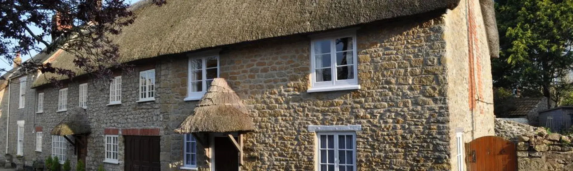 An old stone walled thatched holiday cottage positioned next to a road.