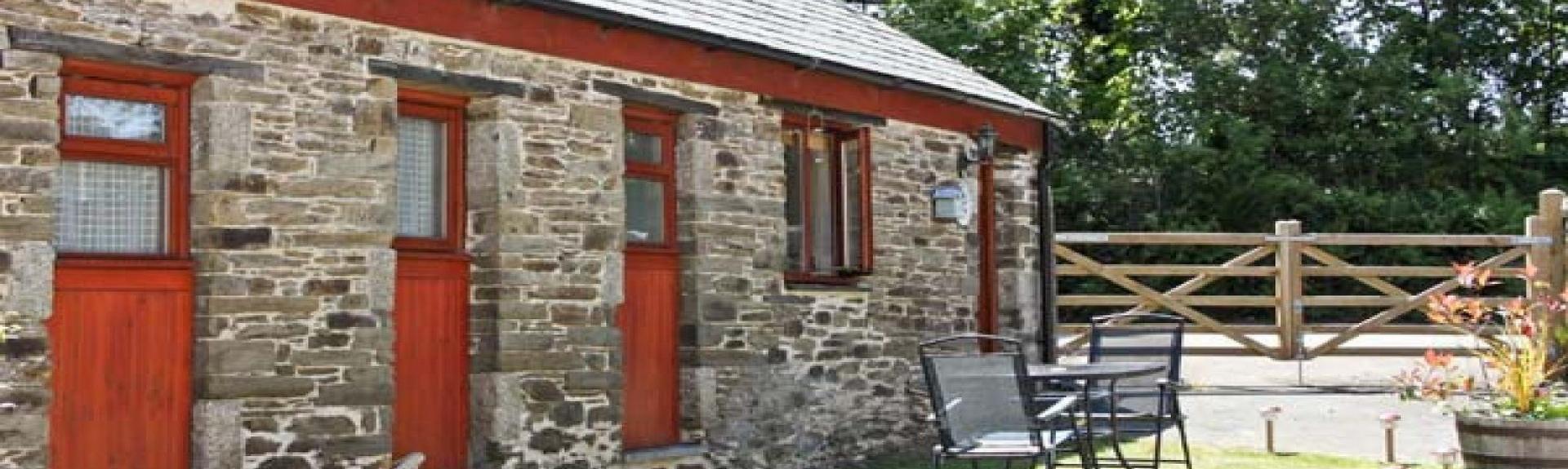 A single storey, stone barn conversion overlooks a lawned garden with outdoor table and chair.