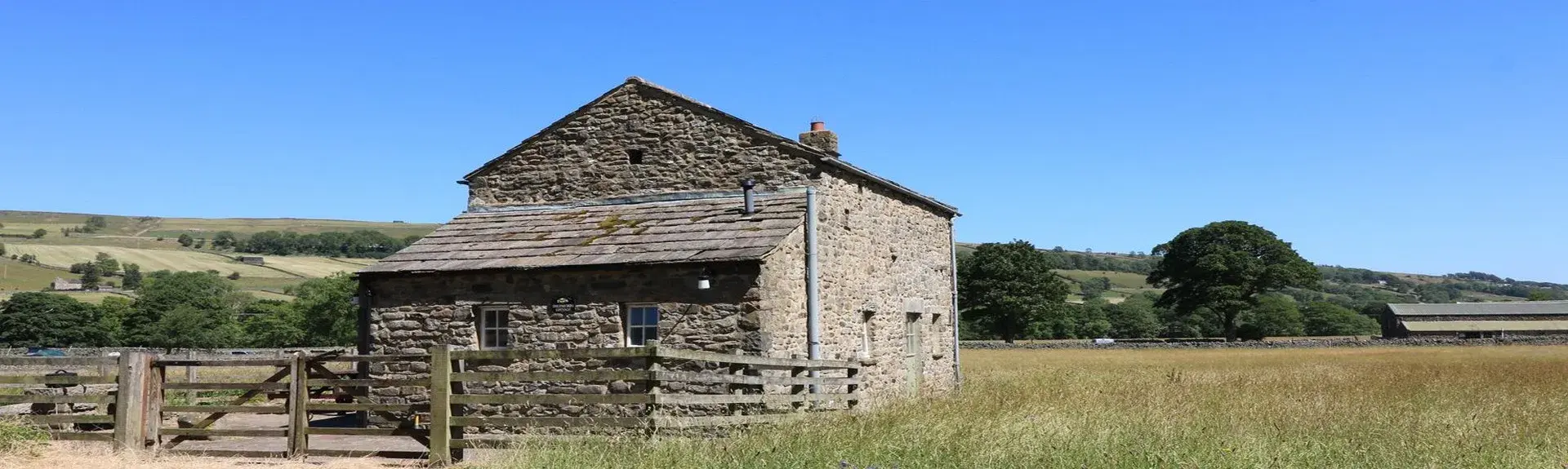 A fenced-in stone-built barn conversion is surrounded by open fields