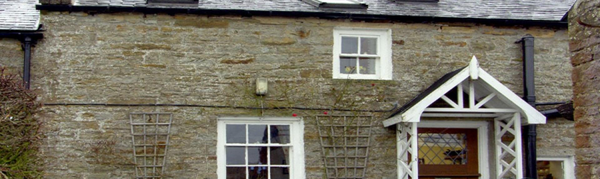 A terraced stone cottage with a low wall around the front garden